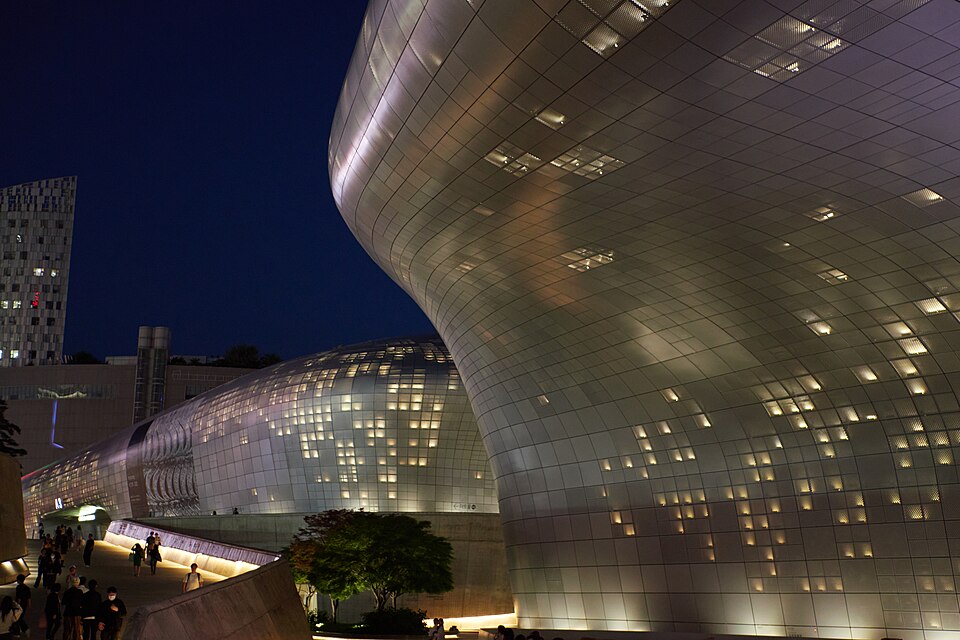 The curved, panelled exterior of Dongdaemun Design Plaza glows with lit windows against a dark night sky.