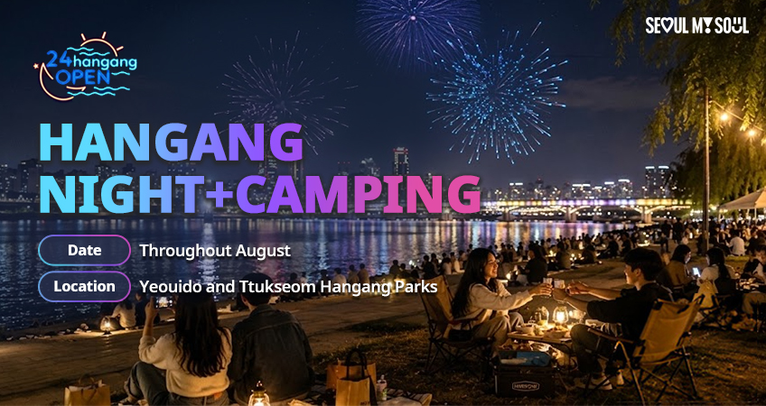 People sit on mats and camping chairs along a riverside at night, with a lit city skyline, bridge, and fireworks bursting overhead.
